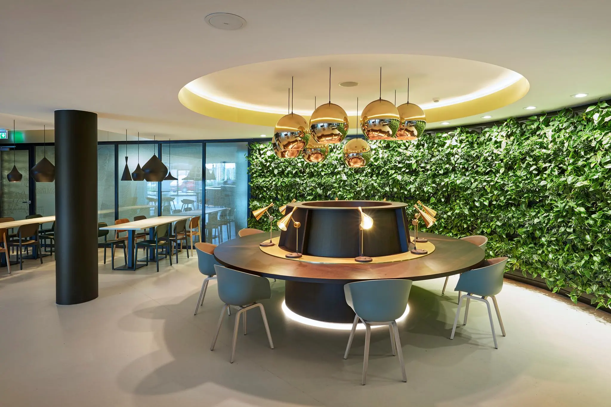 Moderne kantoorruimte aan de Fascinatio Boulevard met ronde werktafel, hanglampen en een groene plantenwand.